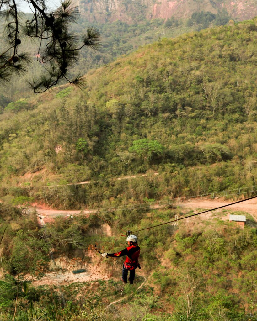 Un guía experimentado demostrando sus habilidades mientras cruza una tirolesa, suspendido sobre un paisaje natural.