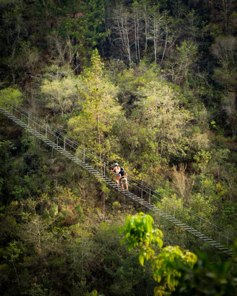 Una persona cruzando una escalera colgante suspendida, rodeada de naturaleza y con un enfoque en la aventura.