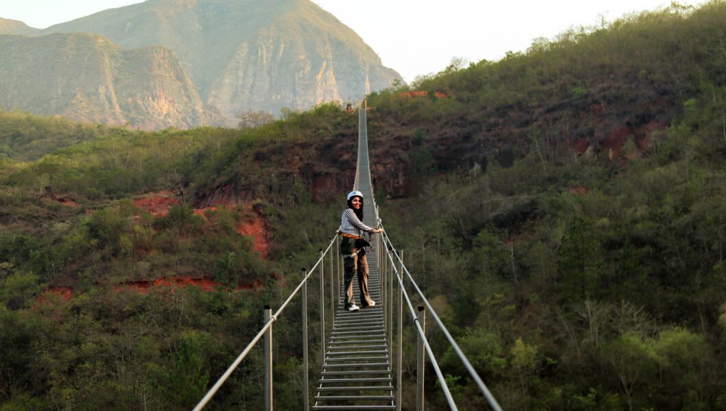 Keisy cruzando la escalera colgante, concentrada y rodeada de un paisaje natural.