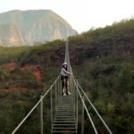 Keisy cruzando la escalera colgante, concentrada y rodeada de un paisaje natural.