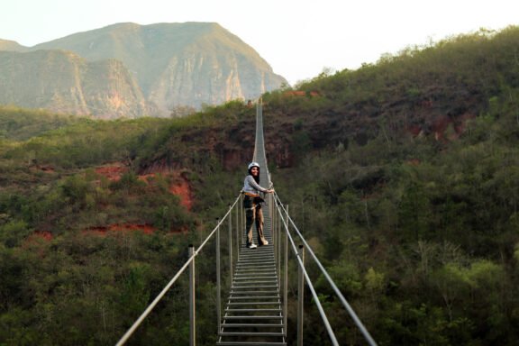 Keisy cruzando la escalera colgante, concentrada y rodeada de un paisaje natural.