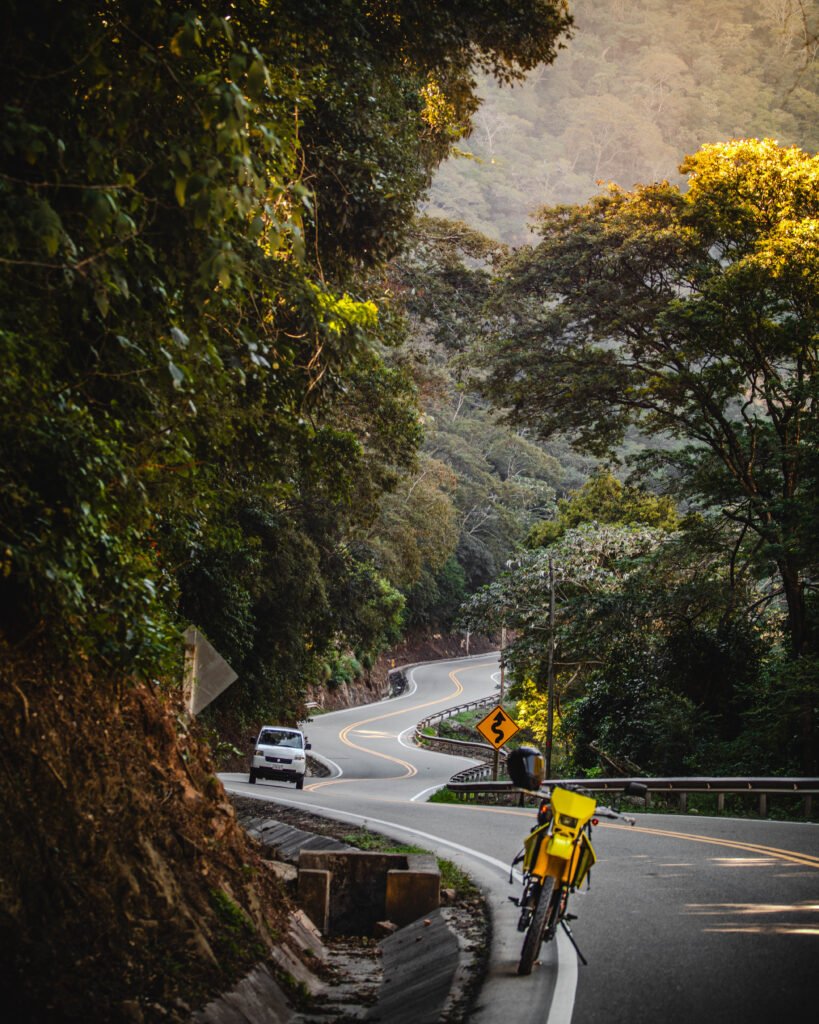 Una carretera serpenteante conocida como "La Viborita", rodeada de densa vegetación, con un automóvil y una motocicleta en el marco, capturada en la ruta hacia los Valles Cruceños.