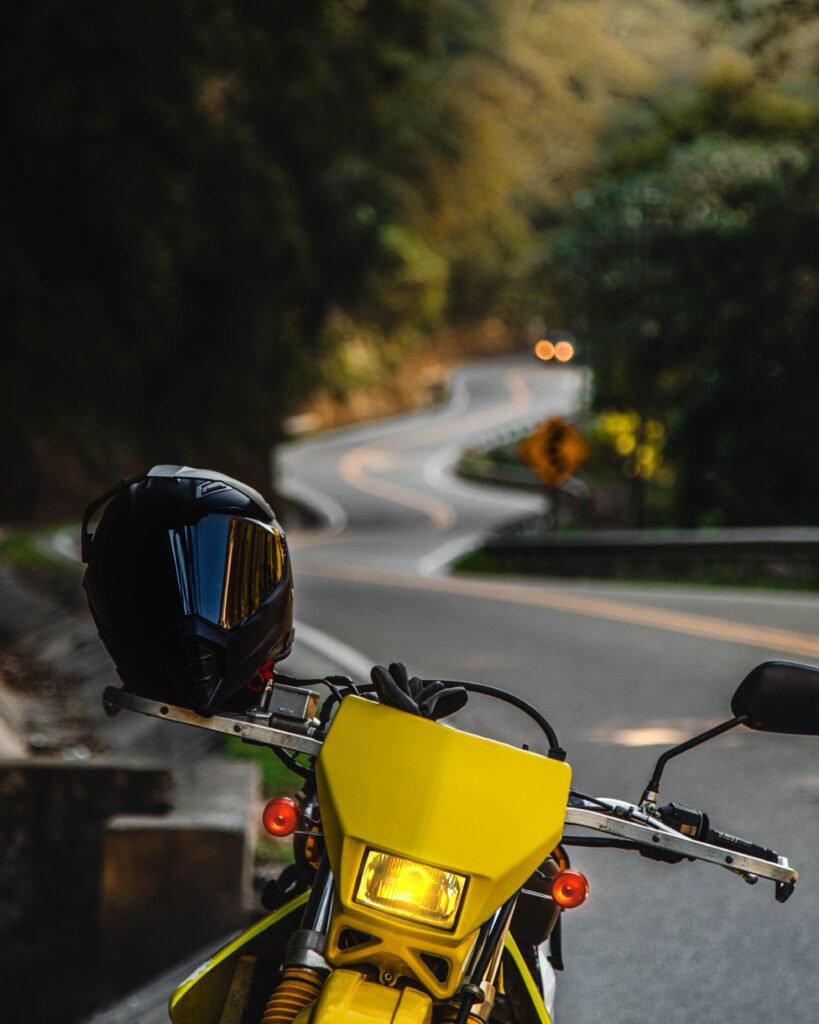 Una motocicleta amarilla con un casco negro en primer plano, estacionada frente a las curvas serpenteantes de "La Viborita", en la carretera a los Valles Cruceños.